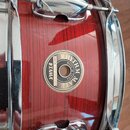 Červený buben s vertikálnímvzorováním a chromovaným kováním. Na korpusu je圆形 štítek s nápisy RHYTHM MATE, MADE IN CHINA, TAMA a SERIAL NO. 1651638. P…
