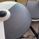 Fotografie zachycuje detail elektronického činely v černo-bílé kombinaci. Povrch je vyroben z gumového materiálu s koncentrickými žebrováním. Na nást…