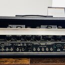 Černý kytarový zesilovač s koženým potahem a madlem. Na předním panelu je nápis DUAL RECTIFIER SOLO HEAD 100 a logo MESA. Jsou zde vidět ovládací prv…