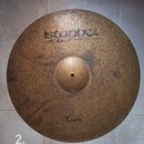 Kruhová mosazná činely s kladeným povrchem. V horní části je černý nápis „istanbul“ a pod ním menší text „Mehmet Handmade cymbals from Turkey“. Ve sp…