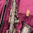 Stříbrný saxofon v otevřeném kufru s fialovou výstuhou. Na zvonu nástroje je nápis „CLASS SUPER Arnati Klasice MADE IN CZECHOSLOVAKIA“. Povrch nástro…
