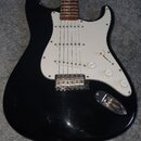 Černá elektrická kytara typu Stratocaster s bílým pickguardem a hnedým hmatníkem. Nástroj má tři jednosmyčkové snímače, jeden přepínač a tři bílé ovl…