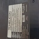 Fotografie zachycuje zadní stranu černého elektronického zařízení s žebrovaným povrchem. Na přístroji je nalepený bílý štítek s texty „THELICON“, „DE…