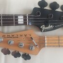 Fotografie zachycuje hlavy dvou basových kytar. Horní je černá s nápisy Fender, DELUXE JAZZ BASS SPECIAL, MADE IN MEXICO a sériovým číslem MXD1901226…