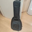 Černý polotvrdý pouzdro (gig bag) na kytaru z textilního materiálu. Na přední části je šedý panel s malým, hnědým oválným logem, které je nečitelné.…