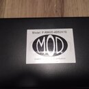 Fotografie zachycuje detail černé povrchové plochy s nalepeným bílým štítkem. Na štítku je uveden nápis Model: P-RMOD-4BB2A1B a výrazné logo MOD v ov…
