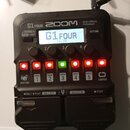 Černý kytarový procesor s nápisy G1 FOUR a ZOOM Multi-Effects Processor. Displej zobrazuje text G1 FOUR v1.10. Zařízení má čtyři otočné ovladače, řad…