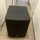 Černý subwoofer s hranatým tvarem a přední textilní maskou. Na horní straně je umístěn kruhový ovládací prvek s několika tlačítky. V dolní části před…