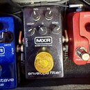 Černý efekt pedál s nápisy MXR, BASSINNOVATIONS a envelope filter. Na horní části jsou čtyři ovládací knoflíky s popisky DRY, FX, DECAY a SENS, upros…