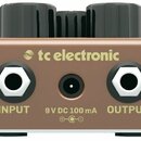 Detailní pohled na zadní stranu kytarového efektu v hnědé barvě. Na šasi je umístěno logo a nápis tc electronic, dva šestihranné konektory s popisky…