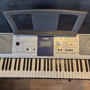 Stříbrný digitální klavír s bílými a černými klávesami. Na horním panelu je vlevo logo YAMAHA a vpravo nápis PSR-325. Nástroj obsahuje displej, řadu…