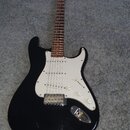 Černá elektrická kytara s bílým pickguardem a hnedým hmatníkem. Na hlavě krku je viditelné logo Fender. Nástroj má tři snímače typu single-coil, tři…