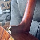 Detailní pohled na spoj krku a korpusu akustické kytary z tmavého dřeva s lesklým povrchem. Na korpusu je vidět kovový薵třpen pro upevnění popruhu. V…