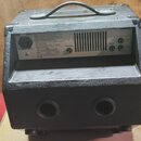 Zadní strana černého komba s povrchem z texturovaného vinylu a přenosnou rukojetí. Na zadním panelu jsou vidět nápisy Head Phones, Speaker Out a vstu…