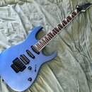 Modrá elektrická kytara s tmavým hmatníkem a černými komponenty. Na hlavě krku je bílý nápis Ibanez. Nástroj má dva humbuckery, jeden ovládací knoflí…