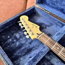 Elektrická kytara v modrém polstrovaném kufru. Na hlavě hmatníku je vidět logo Fender a nápis STRATOCASTER. Hmatník je vyroben z tmavého dřeva s vidi…