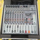 Stříbrný mixážní pult značky behringer, model XENYX X1222USB. Zařízení je umístěno v ochranném černém kufru s pěnovou výplní. Na panelu jsou vidět po…