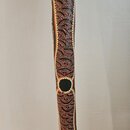 Fotografie zachycuje detail dřevěného didgeridoo. Nástroj je zdobený malbou z drobných teček v červené, žluté a bílé barvě na tmavém podkladu. V doln…