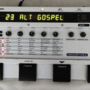 Bílý efektový pedál s nápisem VOCALIST.LIVE 4 a logem DigiTech. Zařízení má digitální displej s žlutým textem 23 ALT GOSPEL, několik ovládacích knofl…