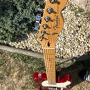 Elektrická kytara s červeným trupem a světle hnědým javorovým hnedkem. Na hlavě hnedku je černé logo Fender a nápis TELECASTER® s menším doplňkem ORI…