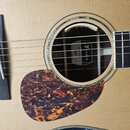Detail akustické kytary s přírodním povrchem desky. Uvnitř ozvučnice je vidět štítek s logem a nápisem 3F FURCH. Kytara má hnědý vzorovaný pickguard…