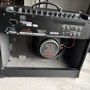 Černý kytarový kombozesilovač s otevřeným zadním panelem. Na zadní straně je štítek s nápisy Roland, AC 230V 50Hz/60Hz, 77W, MODEL: KT-100 a SERIAL N…