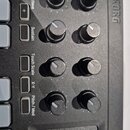 Detailní pohled na ovládací panel černého MIDI kontroléru značky KORG. Jsou vidět čtyři dvojice otočných potenciometrů a sloupec tlačítek s popisky O…