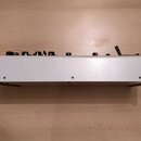 Fotografie zachycuje bílé elektronické zařízení s ovládacími knoflíky na horní straně a dřevěnými bočními panely. Přední strana je hladká, bílá a v d…