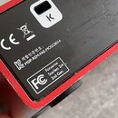 Detail spodní strany červeného zařízení s černým plastovým panelem. Na panelu jsou vidět nápisy „Focusrite Scarlett 2i4 2nd Gen“, logo „FC“ a kód „MS…