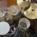 Kytice bubnů v béžové barvě s kovovým kováním a dvěma zlatými činely. Na jednom z činelů je vidět logo Zildjian a nápis S SERIES oraz 20 RIDE, na dru…