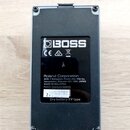 Zadní strana šedého efekt pedálu značky BOSS. Na černém štítku je uveden nápis Roland Corporation, adresa 2036-1 Nakagawa, Hosoe-cho, Kita-ku, Hamama…