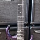Fialová elektrická kytara s tmavým hmatníkem a dvěma humbuckery. Na hlavě je svisle napsáno "Mayones" a nahoře je podpis. Spodní část korpusu obsahuj…