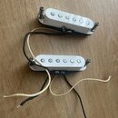 Dvě bílé snímače typu single-coil s pěti viditelnými póly. Snímače mají kovové montážní šrouby a jsou připojeny k černým a bílým vodičům. Na povrchu…