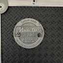 Detailní záběr na kovový štítek připevněný k černému povrchu s protiskluzovým vzorem. Na štítku je nápis „Custom-made“, logo „Music DATA CASES“ a tex…