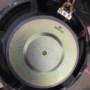Fotografie znázorňuje zadní část reproduktoru s kovovým magnetem zlatavé barvy a černým plastovým rámem. Na zadní straně magnetu je černý nápis „pp-1…