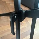 Detail černé kovové konstrukce stojanu s utahovací pákou. Na boku pákového mechanismu je viditelné logo "K&M". Povrch je matně černý s mírnými známka…
