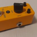 Žlutý efekt pedál s nápisy MOOER, YELLOW COMP, OUTPUT, INPUT, COMP a EQ. Na horní straně se nachází stříbrný spínací pedál, jeden velký černý otočný…