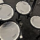 Fotografie zobrazuje čtyři bílé padové bubny elektronické bicí s černými rámy. Na každém padu je vidět logo Roland a nápis V-Drums s drobným textem P…