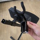 Černý kovový stojan na hudební nástroj s polstrovanou opěrkou v podobě háku. Na rámu je viditelný nápis frame-model. Stojan má hranatou konstrukci a…
