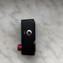 Černý obdélníkový modul s kovovým povrchem. Na boku je umístěn jackový vstup s bílým nápisem INPUT a červený vroubkovaný knoflík. Pravá strana zaříze…
