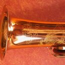 Zlatý saxofon s gravírovaným ornamentem na korunu. Na povrchu je vyryt nápis „KULINS WARTH SM90“. Nástroj vykazuje známky používání v podobě drobných…