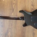 Zadní strana elektrické kytary v černé barvě s lesklým povrchem. Na zadní straně krku je viditelný nápis „Made by the PRS Musical Instruments Co., Lt…
