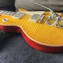 Elektrická kytara s žlutým plamenovitým topem a červenými boky. Na kytaru je instalován chromovaný Bigsby vibrační systém s nápisem „Bigsby“. Nástroj…