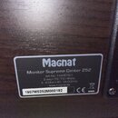 Fotografie detailu tmavého dřevěného povrchu s nalepeným informativním štítkem. Na štítku je uveden název značky Magnat a model Monitor Supreme Cente…