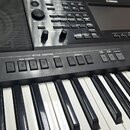 Černý digitální klavír s bílými a černými klávesami. Na ovládacím panelu je nápis YAMAHA a sekce STYLE CONTROL s tlačítky označenými jako INTRO, MAIN…