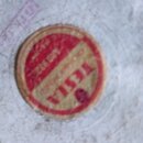 Fotografie zachycuje detail středového štítku vinylové desky. Štítek je červenobílý s nápisem TESLA a nečitelnými texty v horní části. Povrch desky i…