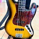 Elektrická basová kytara s korpusem v barevném přechodu od žluté k černé (sunburst). Nástroj má hnědý hmatník s bílými tečkami a tmře červeně vzorova…