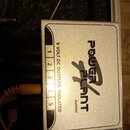 Stříbrný kovový napájecí zdroj s nápisem POWER PLANT Junior. Na boku je vidět pět očíslovaných výstupů s textem 9 VOLT DC OUTPUTS - ISOLATED. Povrch…