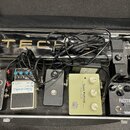 V otevřeném kufru je umístěno pět efektových pedálů a bezdrátový systém. Zleva doprava jsou vidět pedály s nápisy „DITTO STEREO LOOPER tc electronic“…