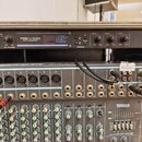 Fotografie zachycuje tři rackové zařízení v šedém case. Horní jednotka je digitální reverb s nápisem REV100 DIGITAL REVERBERATOR. Prostřední zařízení…